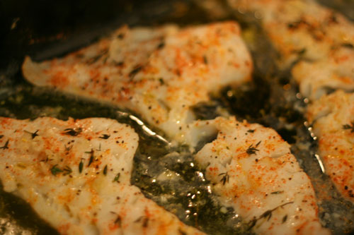 Cod, dusted with red paprika and thyme leaves, is on a baking sheet, cooked and ready to be eaten.