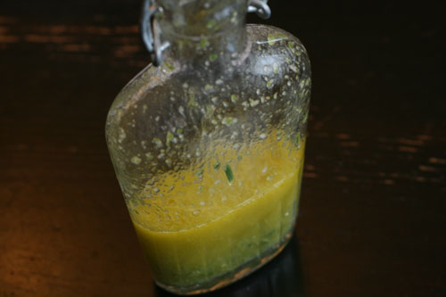 Lemon Rosemary Vinaigrette is shown in a glass bottle on a wooden table.