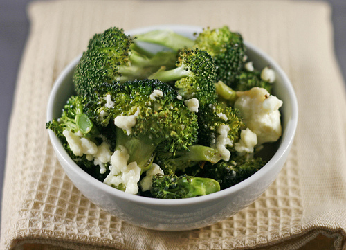 A white bowl of green roasted broccoli and white feta, both with bites of brown caramelization.