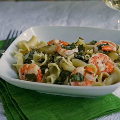 Summer Pasta with Shrimp and Kale is shown in a white bowl set on a green napkin.