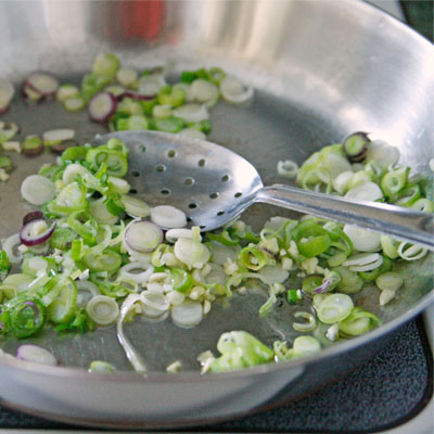 scallions are being sauteed in a stainless steel skillet