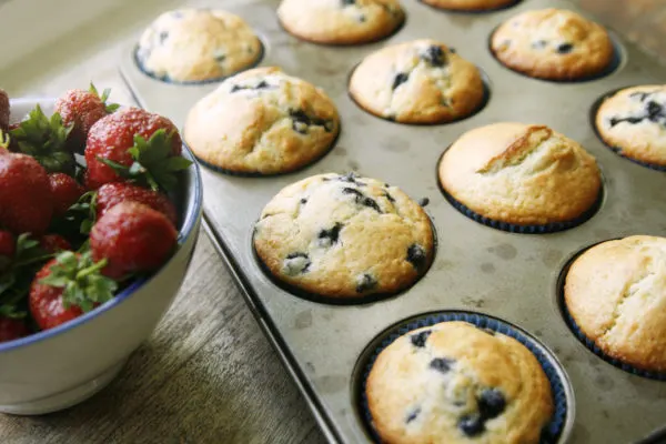 Build a better breakfast with these hot from the oven blueberry muffins still in the muffin tin next to a bowl of strawberries