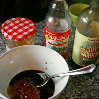 Soy sauce, seasoned rice vinegar and orange marmalade sit on a counter near a bowl containing all three. There's a spoon in the bowl.
