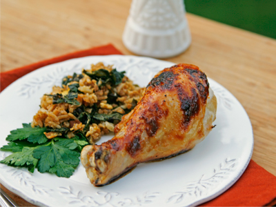 A chicken drumstick that's orange, with browned spots, sits on a white plate with rice dotted with greens nearby.