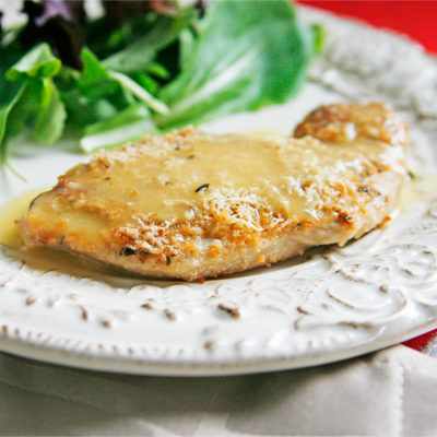 A Rosemary Romano Roasted Turkey Cutlet sits on a cream colored plate with salad nearby. 