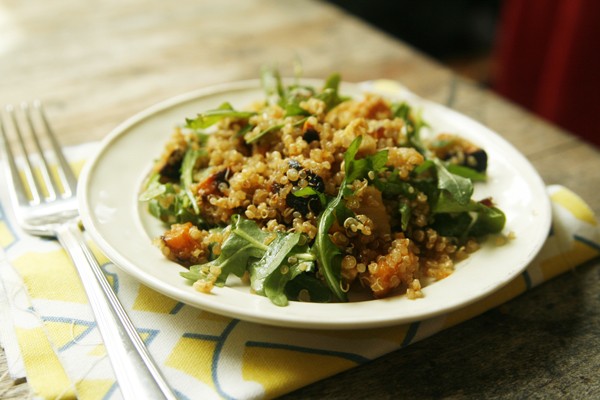 A plate with a salad featuring arugula, grains and other ingredients sits on a yellow napkin with a fork nearby.