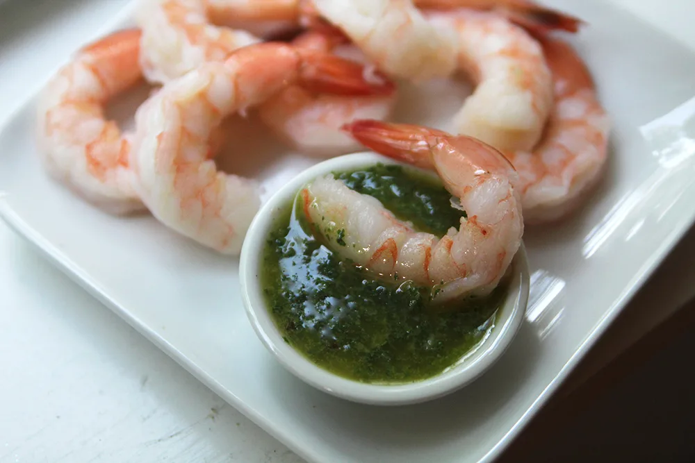 a plate of shrimp with one shrimp in a small bowl of green sauce