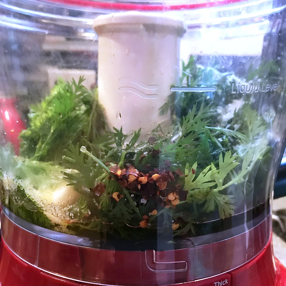 carrot greens, garlic, crushed red peppers and other ingredients are shown in a red food processor