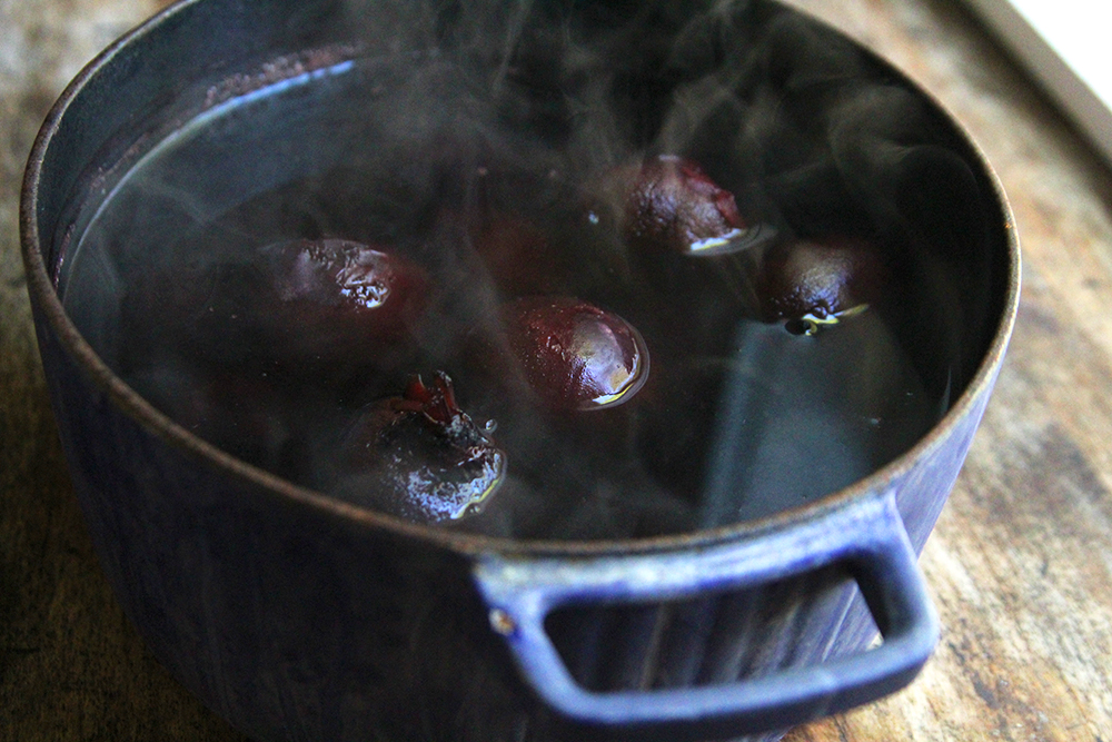 A blue pot holds steaming water and whole beets. 