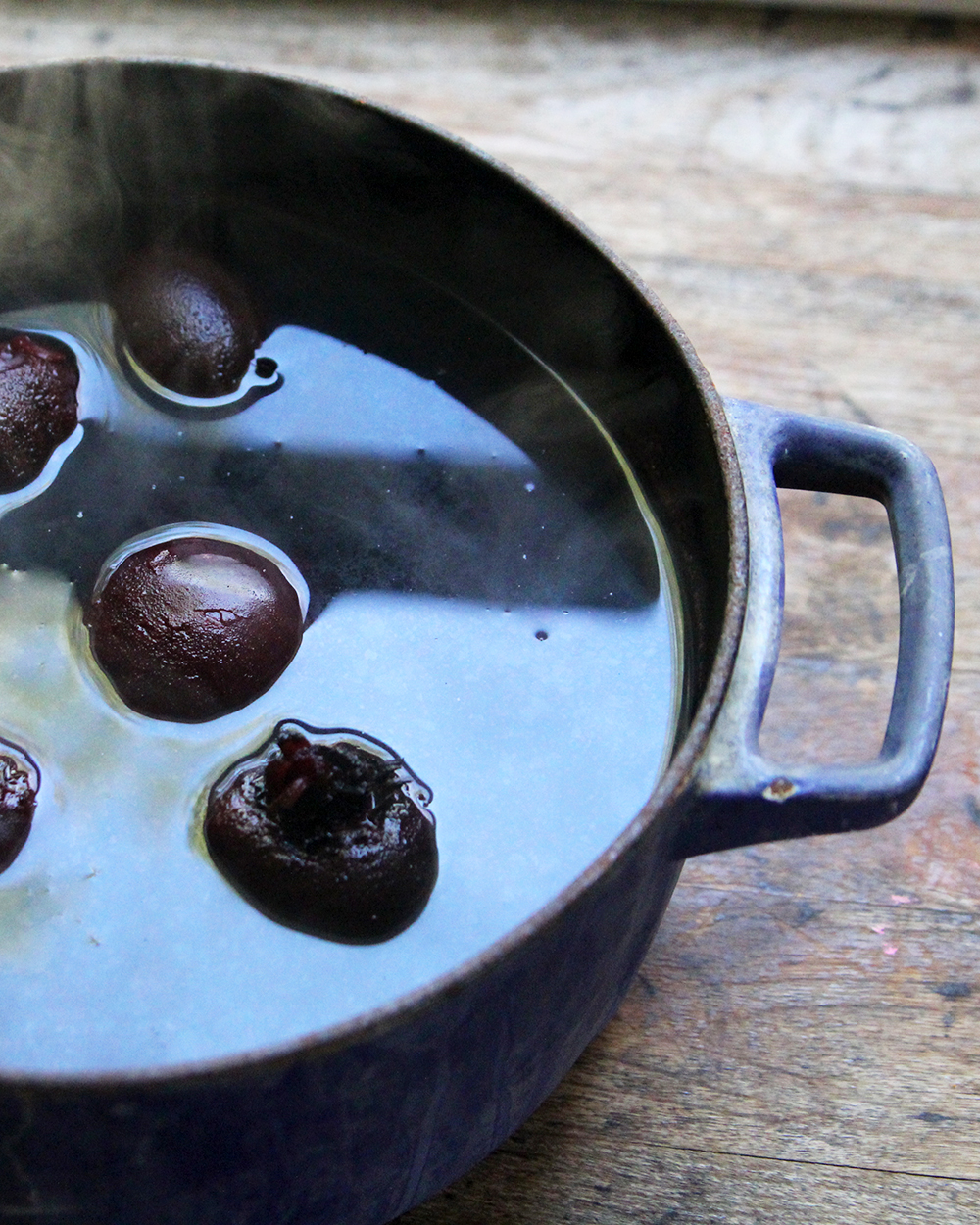A blue pot is shown on a wooden counter. It's filled with beets submerged in water. 