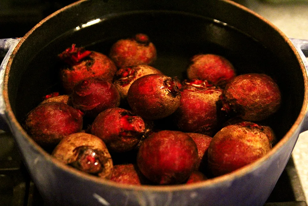A blue pot is shown on a stove. It's filled with beets and water.