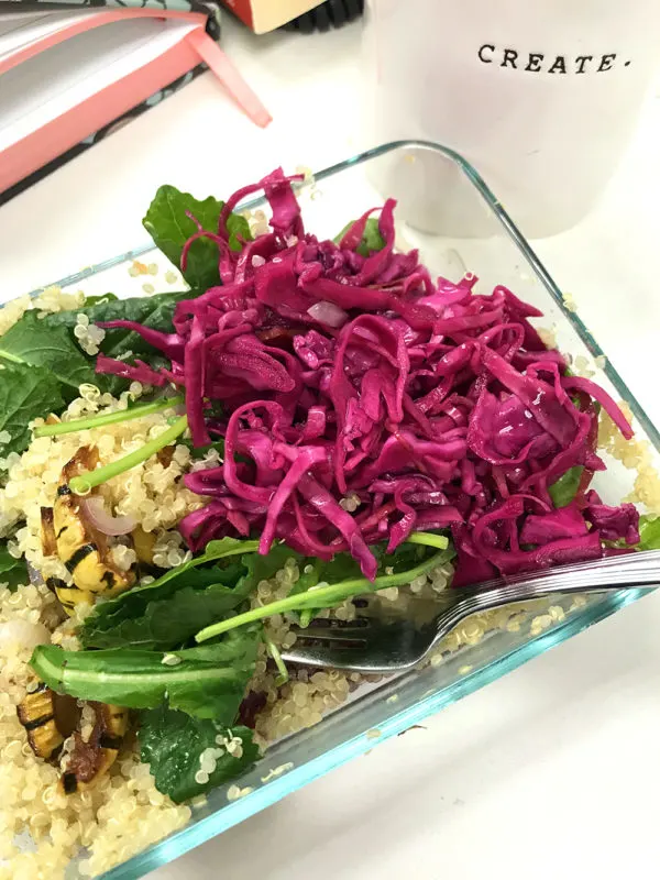A meal prep bowl with a grain, arugula and picked red cabbage sits on a desk.