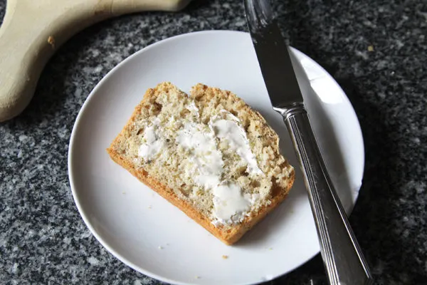 A buttered slice of garlic herb no-knead bread is shown on a white plate. 