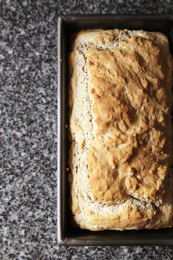 A loaf of garlic herb no-knead bread is shown in a loaf pan on a granite countertop. Bread recipes using self-rising flour use a carbonated agent like beer to activate the rising process.