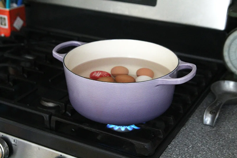 A pot is shown on the stove with water and eggs inside.