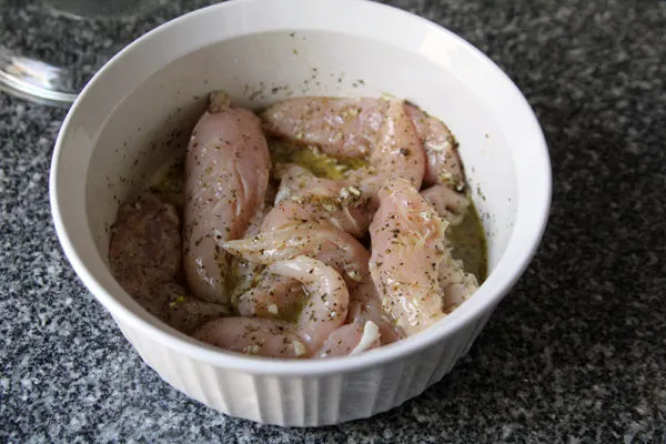 Raw chicken is shown in a white bowl with marinade. The marinade is yellow and herby.