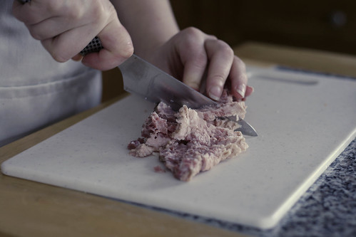 A person (only the hands are showing) cuts corned beef hash on a white cutting board.