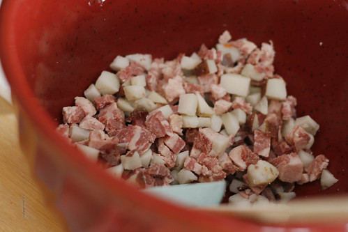 A red bowl containing diced corned beef and potatoes sits on a countertop.