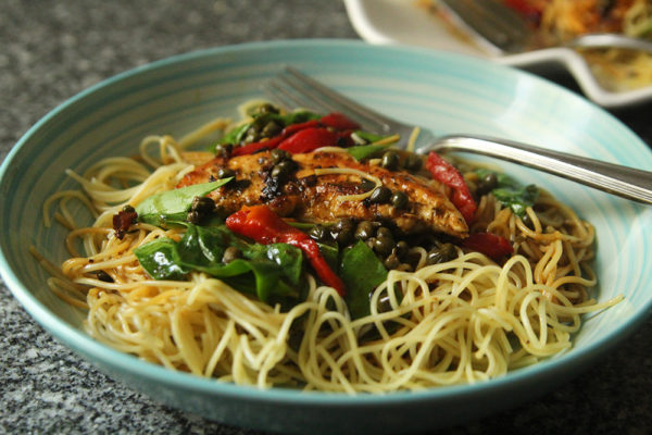A bowl of Chicken, Greens and Roasted Red Peppers with Lemon Butter Caper Sauce over Angel Hair Pasta