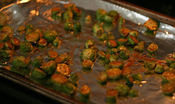 Halved Brussels sprouts are shown on a foil-lined baking sheet in an oven. You can see spots of brown on them.