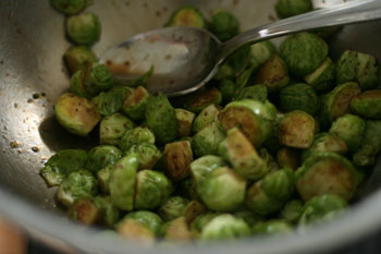 Halved Brussels sprouts are shown in a mixing bowl. They are being mixed with balsamic vinegar and olive oil.