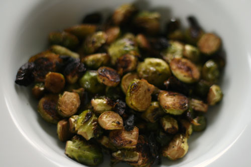 Halved Brussels sprouts are shown in a white bowl. The Brussels sprouts are browned in places from roasting.
