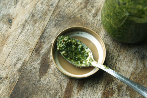 Basil Pecan Pesto coats a spoon that sits in the lid of a jar. The jar is nearby.