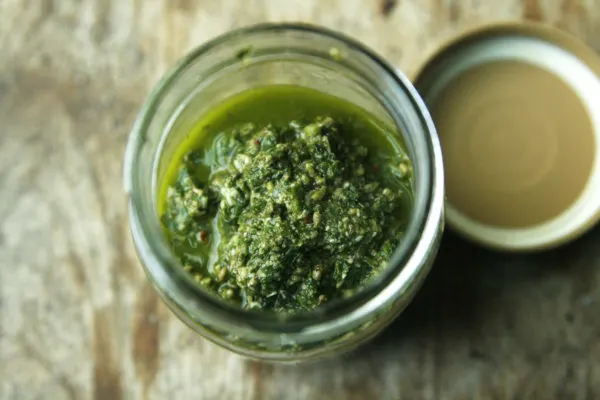 A jar of Basil Pecan Pesto is shown with the lid beside it. This can be made with fresh basil from the farmers market or your garden.