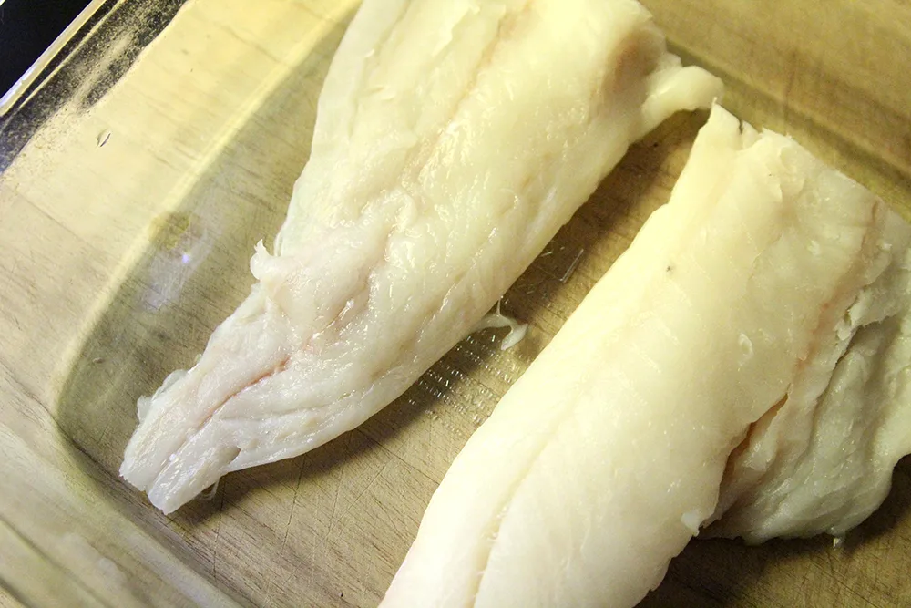 Two haddock fillets are shown in a glass pan on a wooden surface.