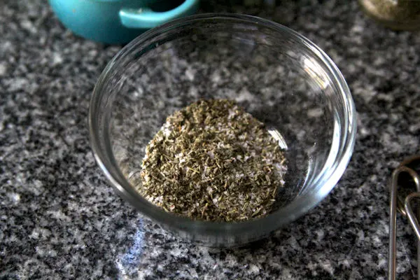 A small glass bowl containing herbs and spices is shown on a granite countertop.