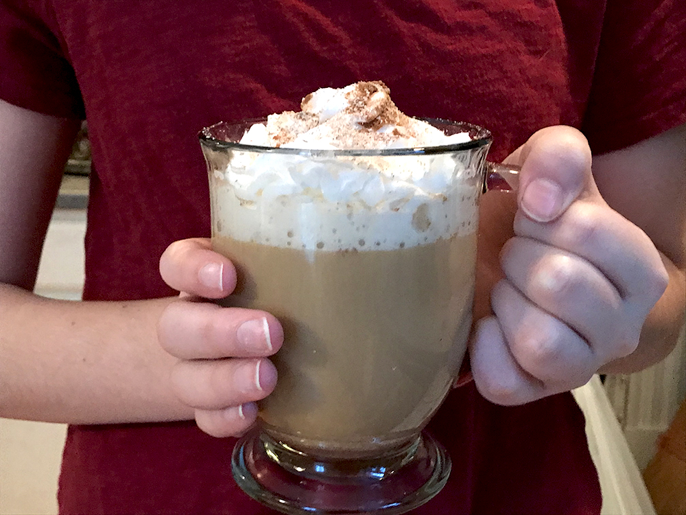how to make eggnog coffee - Hands holding a coffee mug with a coffee drink topped with whipped cream