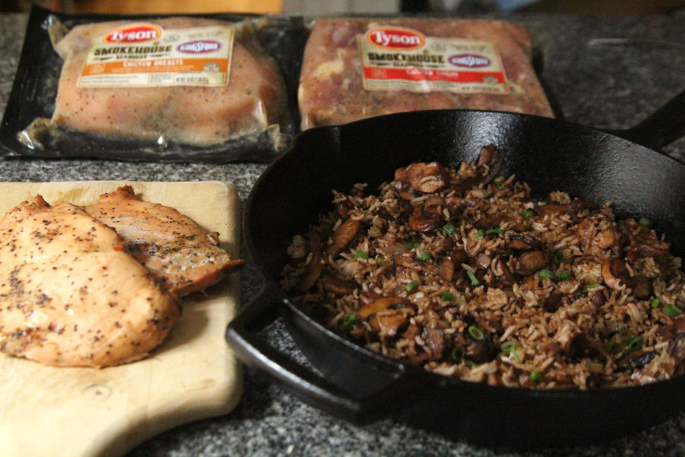 Cooked chicken breasts, a skillet of rice with mushrooms and shallots, two packages of marinated chicken