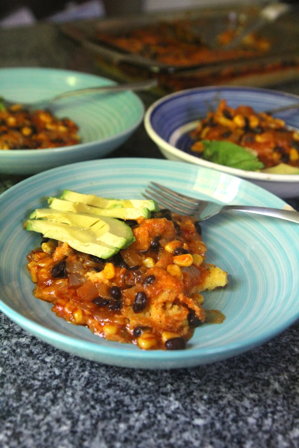 Black Bean Corn Enchilada Pie is shown in three bowls with slices of avocado.