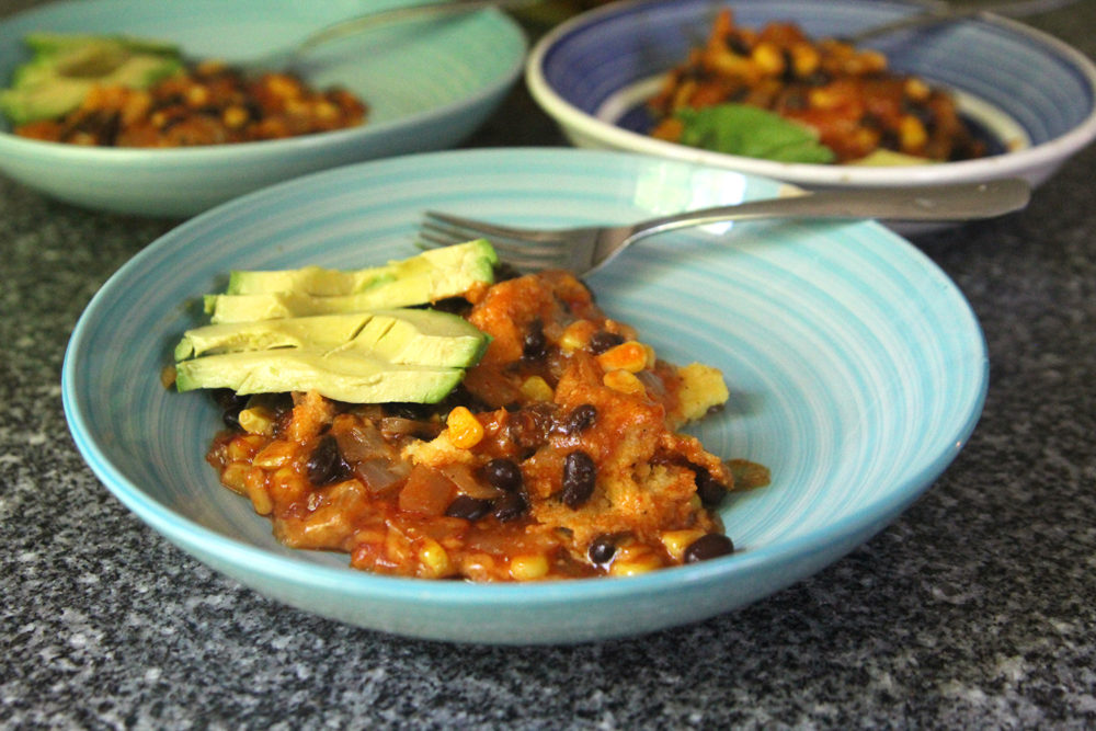 Bowls of Black Bean Enchilada Pie with avocado are shown on a granite countertop.