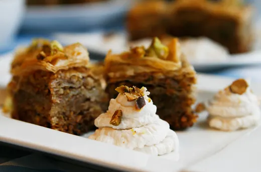 A closeup of cinnamon whipped cream on a white plate with Pistachio Walnut Honey Baklava in the background.