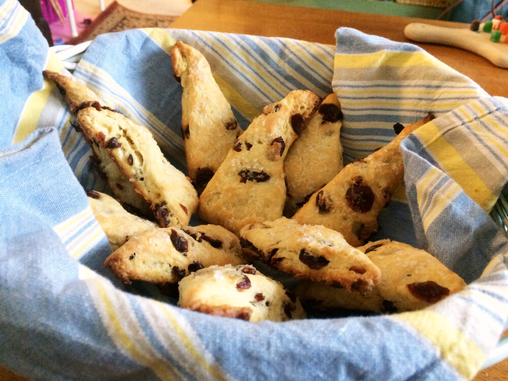 A basket with a blue and yellow striped napkin holds dried cranberry scones.