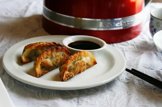 Golden brown gyoza sit on a white plate with a small bowl of soy sauce.
