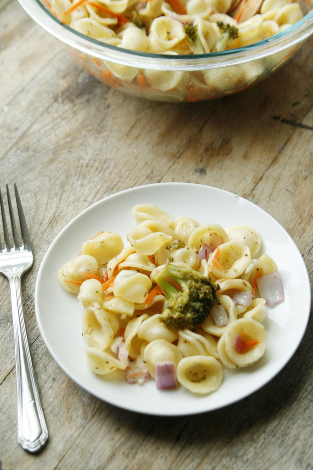 Orecchiette Pasta Salad with Lemon and Oregano is shown on a white plate with a silver fork on a wooden table.