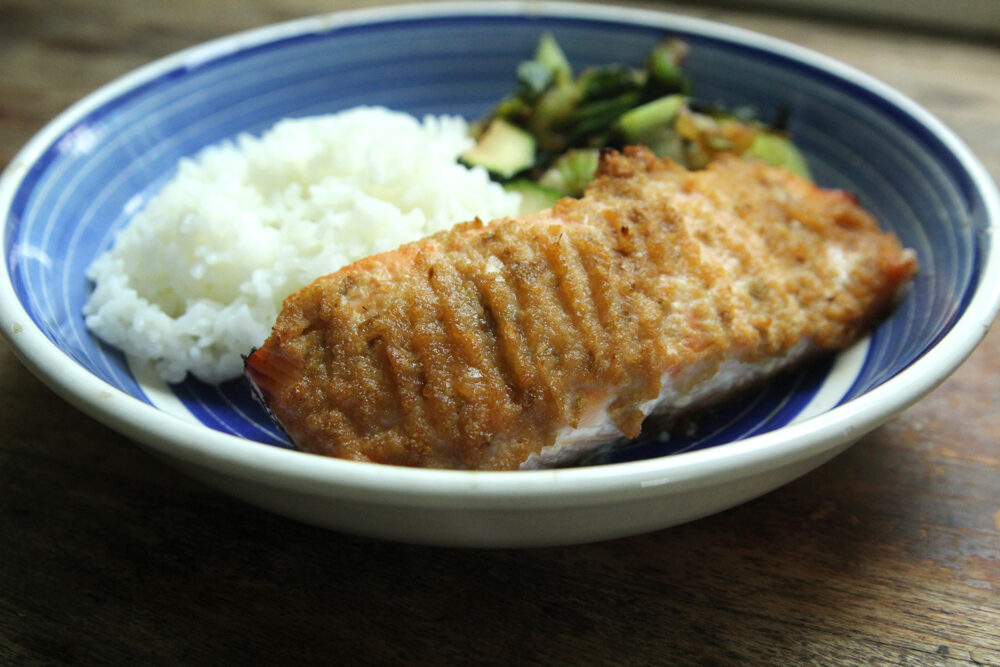 A salmon fillet is shown in a blue bowl with white rice and green vegetables. This salmon has been marinated in bulgogi marinade.