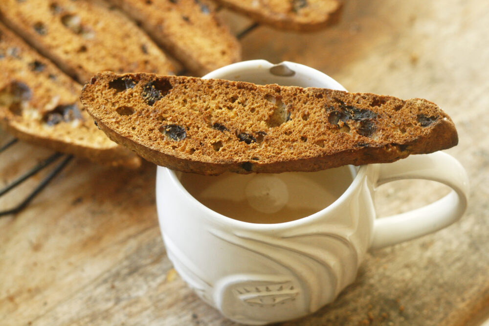 A slice of blueberry biscotti is balanced on a coffee cup.