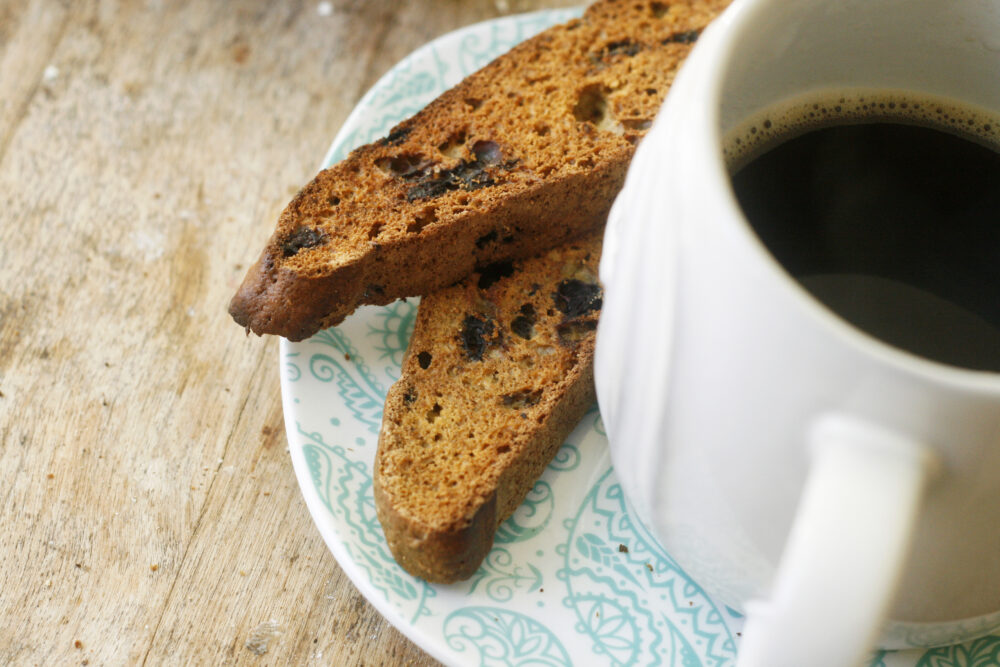 Two Wild Blueberry Biscotti cookies sit on a plate with a coffee nearby.