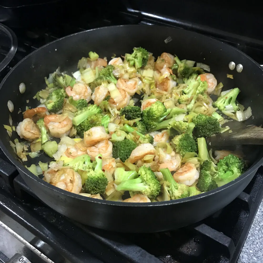 Easy Garlicky Leek, Broccoli and Shrimp Stir-Fry is down in a dark-colored skillet on the stove.
