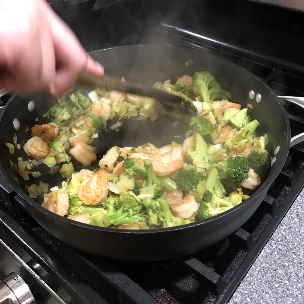 Easy Garlicky Leek, Broccoli and Shrimp Stir-Fry is shown over rice in a blue bowl on a grey granite countertop with a silver fork.