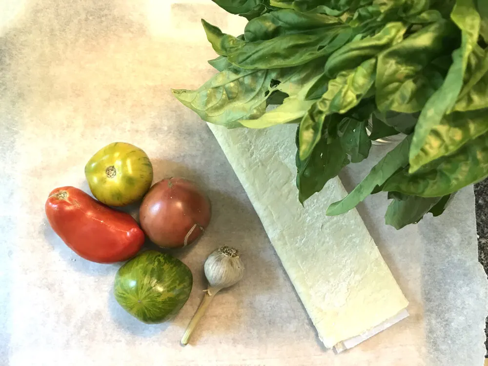 Ingredients for a Tomato Basil Tart are shown: puff pastry, tomatoes, garlic and basil