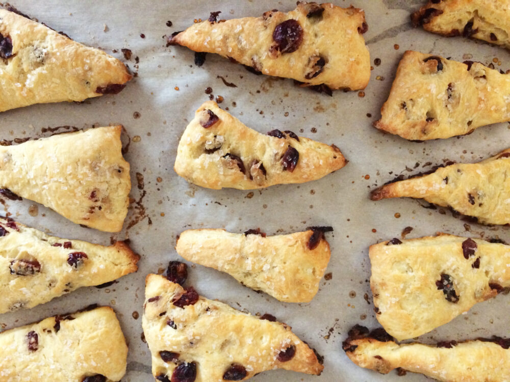 Dried cranberry scones sit on a parchment-lined baking sheet.