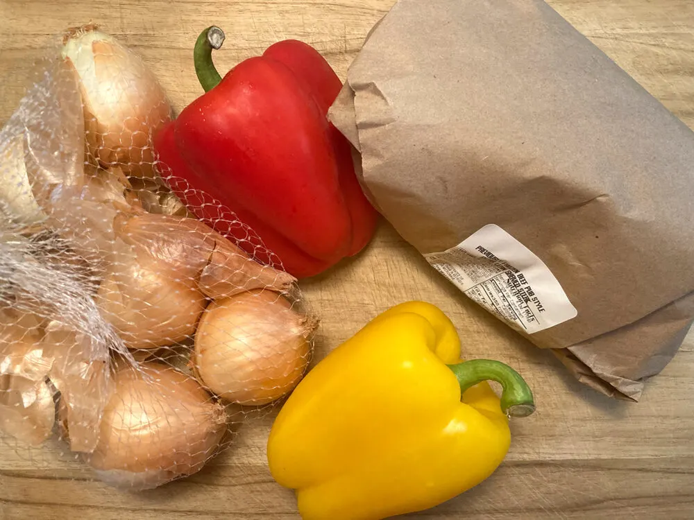 A brown paper wrapped bundle is shown with a red pepper, yellow pepper and onions.