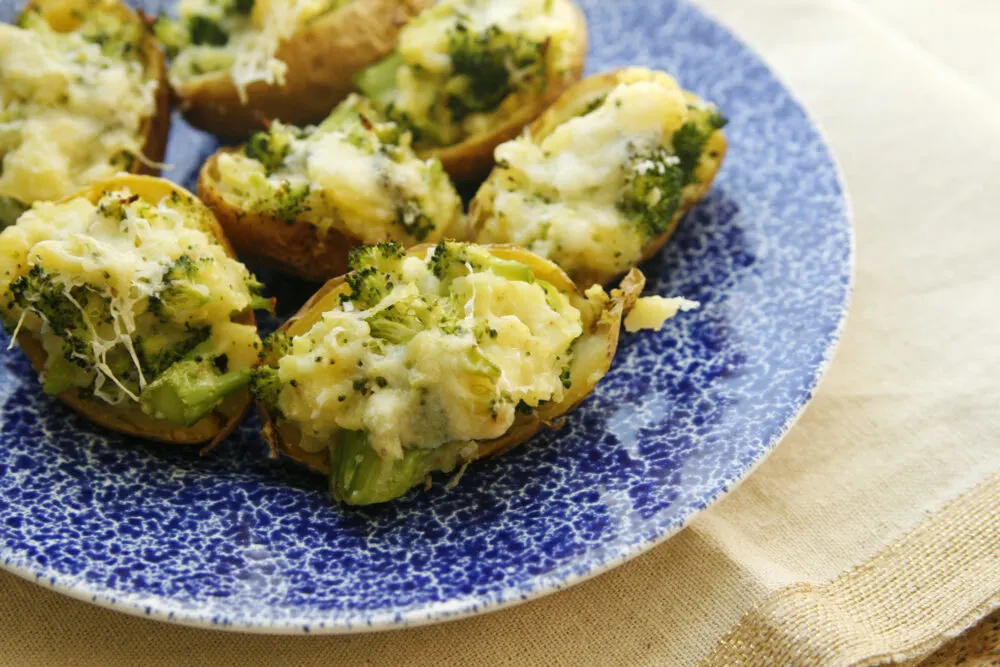Broccoli and cheese filled potatoes sit on a blue and white plate on top of a tan table runner.