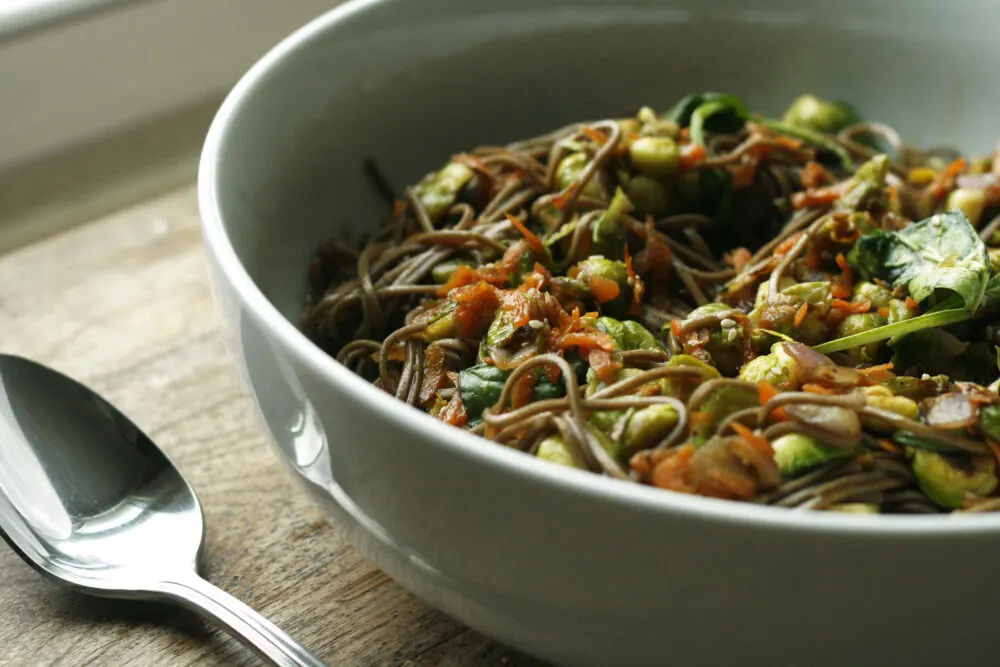 Sesame Soba Noodles with Brussels Sprouts in a white bowl on a distressed wooden table.