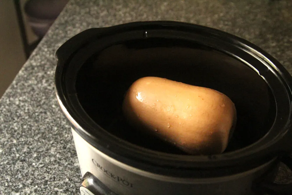 A butternut squash sit in the bowl of a slow cooker on a granite countertop.