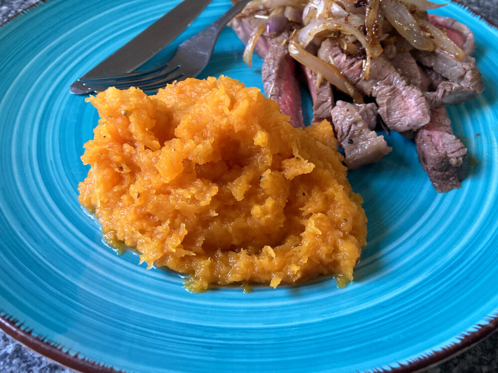 Slow cooker butternut squash puree on a turquoise plate with steak and onions. 